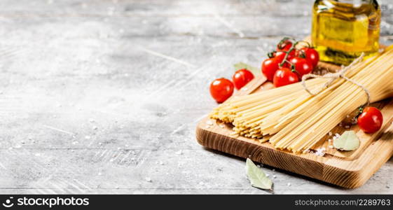 Spaghetti dry on a wooden cutting board with tomatoes. On a gray background. High quality photo. Spaghetti dry on a wooden cutting board with tomatoes.