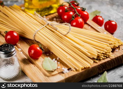 Spaghetti dry on a wooden cutting board with tomatoes. On a gray background. High quality photo. Spaghetti dry on a wooden cutting board with tomatoes.
