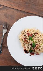 Spaghetti pasta bacon with dried spicy chilli on white plate on the wood table from top view