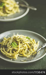 Spaghetti pasta bucatini with pesto sauce and parmesan. Italian traditional perciatelli pasta by genovese pesto sauce in two ray dishes. Dark green concrete surface, rustic style, close up