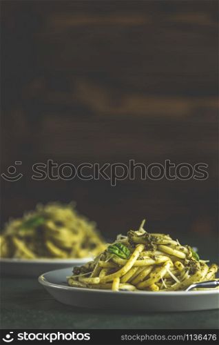 Spaghetti pasta bucatini with pesto sauce and parmesan. Italian traditional perciatelli pasta by genovese pesto sauce in two ray dishes. Dark green concrete surface, rustic style, close up