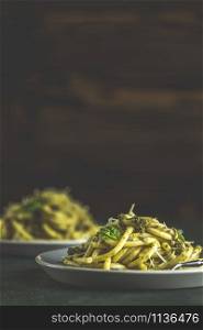 Spaghetti pasta bucatini with pesto sauce and parmesan. Italian traditional perciatelli pasta by genovese pesto sauce in two ray dishes. Dark green concrete surface, rustic style, close up