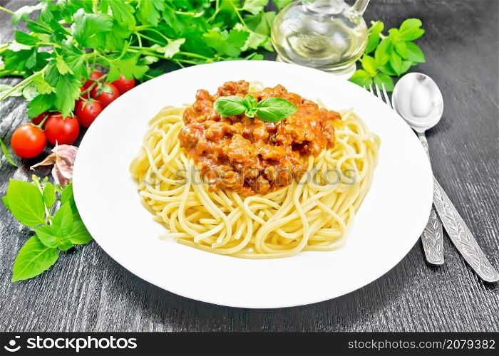 Spaghetti pasta with Bolognese sauce of minced meat, tomato juice, garlic, wine and spices in a plate, vegetable oil, spicy herb on black wooden board background