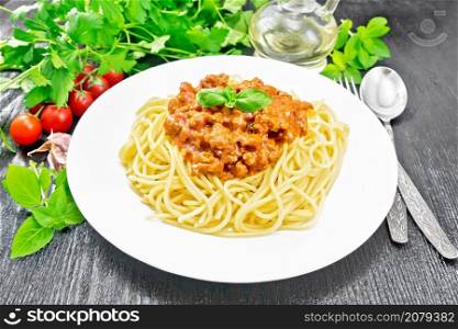 Spaghetti pasta with Bolognese sauce of minced meat, tomato juice, garlic, wine and spices in a plate, vegetable oil, spicy herb on black wooden board background