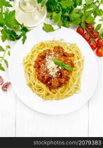 Spaghetti pasta with Bolognese sauce of minced meat, tomato juice, garlic, wine and spices with cheese in a plate, vegetable oil, spicy herb on a light wooden board background from above