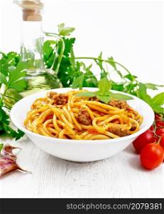 Spaghetti pasta with sauce Bolognese of minced meat, tomato juice, garlic, wine and basil in a plate, vegetable oil, spicy herb on a white wooden board background