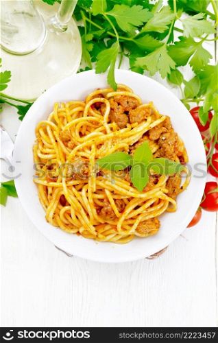 Spaghetti pasta with sauce Bolognese of minced meat, tomato juice, garlic, wine and basil in a plate, vegetable oil, spicy herb on a light wooden board background from above 