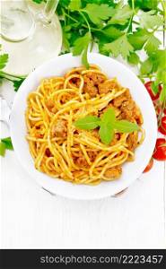 Spaghetti pasta with sauce Bolognese of minced meat, tomato juice, garlic, wine and basil in a plate, vegetable oil, spicy herb on a light wooden board background from above 