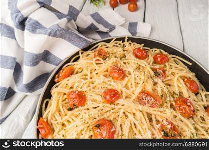 Spaghetti pasta with tomatoes and parsley on wooden table.