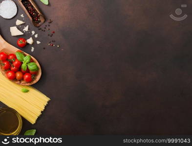 Spaghetti with cherry tomatoes in wooden bowl with pepper in scoop and parmesan cheese with salt on dark brown table background. Space for text