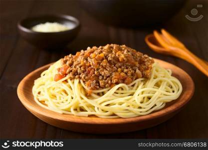 Spaghetti with homemade bolognese sauce made of fresh tomato, mincemeat, onion, garlic and carrot, served on wooden plate with grated cheese in the back, photographed with natural light (Selective Focus, Focus in the middle of the image)