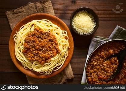 Spaghetti with homemade bolognese sauce made of fresh tomato, mincemeat, onion, garlic and carrot, served on wooden plate with grated cheese and skillet with sauce on the side, photographed overhead with natural light