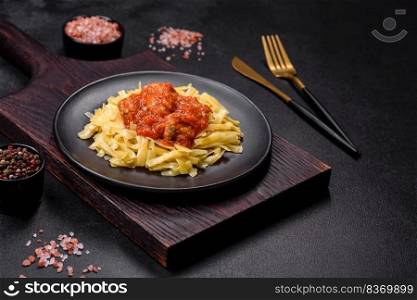 Spaghetti with meat balls in tomato sauce in a black bowl on a dark concrete background. Pasta with beef meatballs in tomato sauce with spices and herbs on a dark background