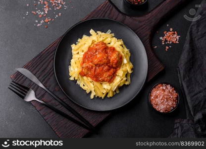 Spaghetti with meat balls in tomato sauce in a black bowl on a dark concrete background. Pasta with beef meatballs in tomato sauce with spices and herbs on a dark background