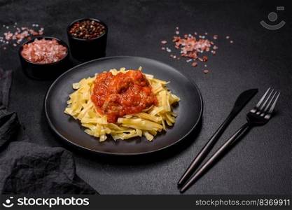 Spaghetti with meat balls in tomato sauce in a black bowl on a dark concrete background. Pasta with beef meatballs in tomato sauce with spices and herbs on a dark background
