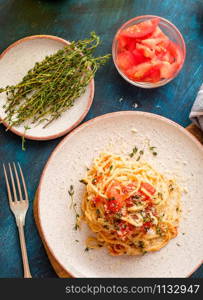 Spaghetti with tomatoes and thyme in a plate on a blue table. Top view.