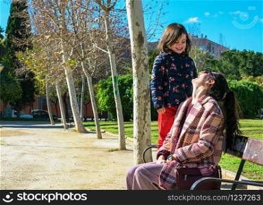 Spain / Murcia - February 2 of 2019: Mother and daughter looking each other and laughing on a bench at a natural park in Murcia.. Portrait of mother and daughter looking each other and laughing