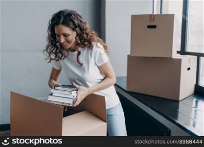 Spanish girl in white t-shirt packing books. Carefree young european woman unpacking boxes. Cheerful student goes to university. Relocation and independence concept.. Spanish girl in t-shirt packing books. Carefree student goes to university. Relocation concept.