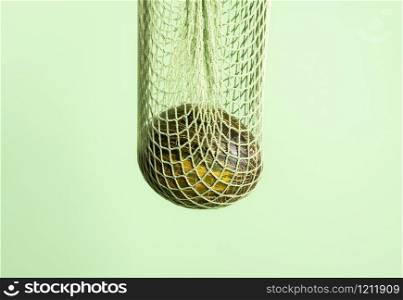 Spanish melon hanging in a net bag on a green seamless background. Frog skin melon in mesh fabric shopping bag. Buying healthy food. Fresh fruit.