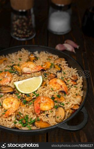 Spanish paella with shellfish and prawns on wooden table, rustic