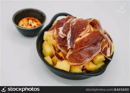 Spanish patatas bravas ration with Iberian cured ham