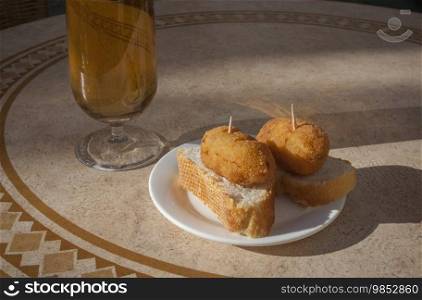 Spanish pinchos of croquettes close to glass of beer. Pincho served over sunny terrace table