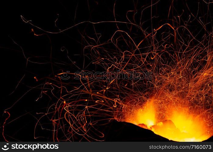 Sparking of burning charcoal spread on dark background.