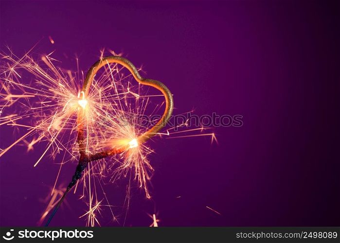 Sparkler in love heart shape on a purple background with lots of sparks. Wedding or Valentine&rsquo;s day celebration banner with copy-space..