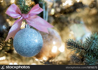 Sparkling Christmas bauble with pink bow hanging in decorated tree, copy space and bokeh light background, Holiday concept space for text. Sparkling Christmas bauble with pink bow hanging in decorated tree, copy space and bokeh light background, Holiday concept