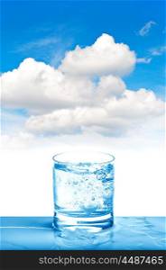 Sparkling water in glass on blue sky background. Fresh cold drink