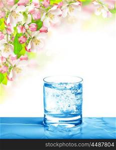 Sparkling water in glass over bright nature background. Cold drink and spring flowers