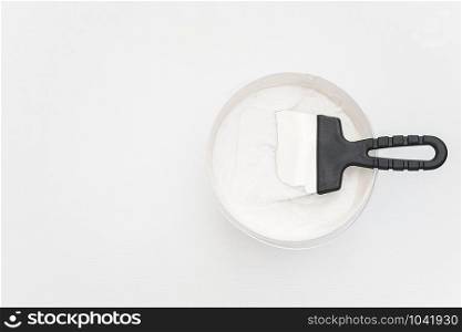 Spatula and a bucket of putty on white wooden boards. Top view Copy space.. Spatula and a bucket of putty on white wooden boards. Top view Copy space