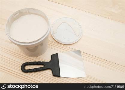 Spatula and a bucket of white putty on wooden boards with copy space.. Spatula and a bucket of white putty on wooden boards with copy space