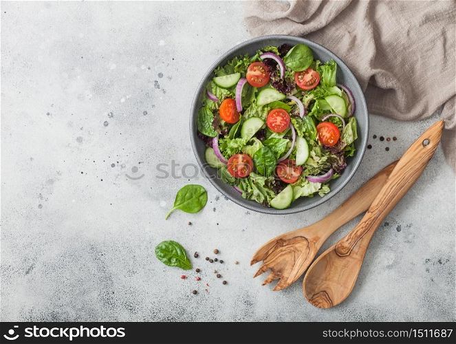 Spatula fork and spoon with bowl of healthy vegetarian vegetables salad with tomatoes and cucumber, lettuce and spinach on light kitchen background. Top view