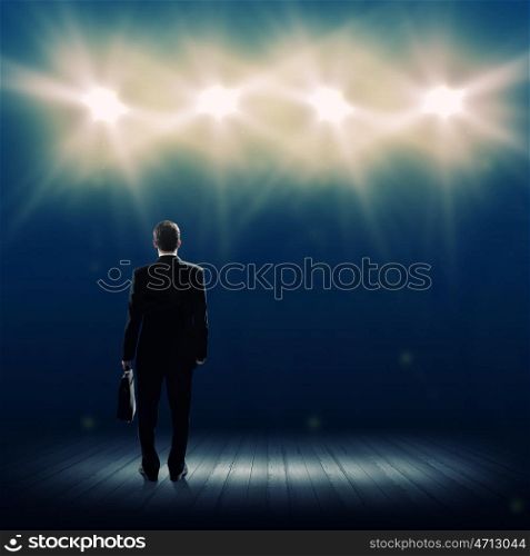 Speaker on stage. Rear view of businessman standing in lights of stage