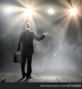 Speaker on stage. Rear view of businessman standing in lights of stage