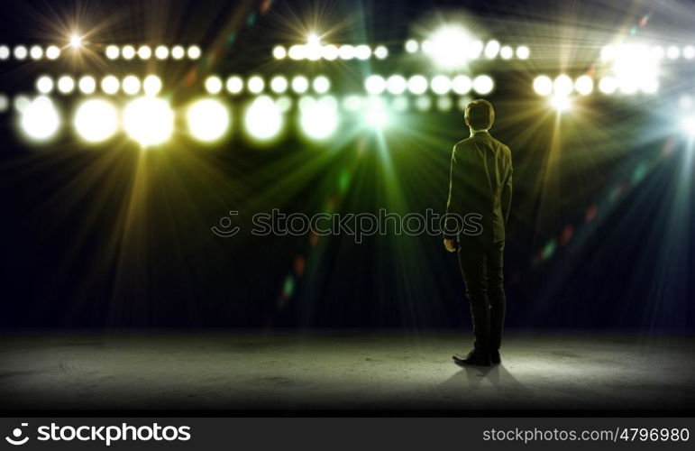 Speaker on stage. Rear view of businessman standing in lights of stage