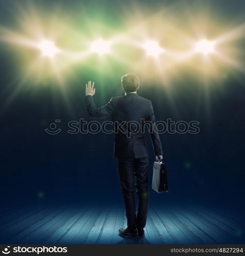 Speaker on stage. Rear view of businessman standing in lights of stage