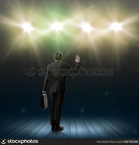 Speaker on stage. Rear view of businessman standing in lights of stage
