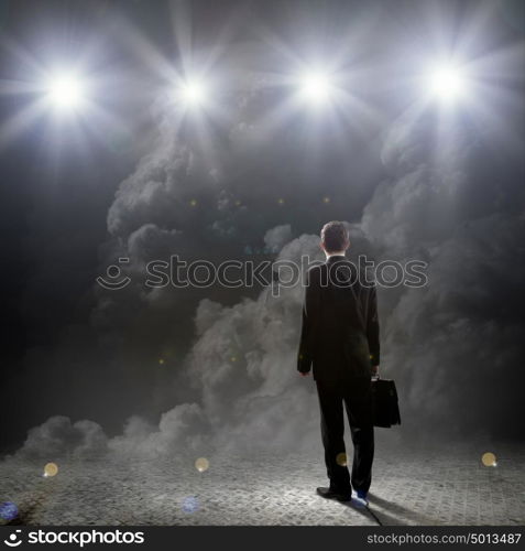 Speaker on stage. Rear view of businessman standing in lights of stage