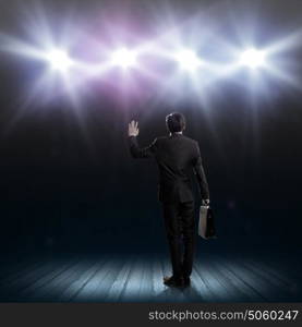 Speaker on stage. Rear view of businessman standing in lights of stage