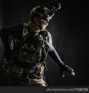 Special operations fighter in helmet with night-vision, thermal imaging device, load carrier carefully moving with caution in darkness, holding hand on pistol, ready for fight during dangerous mission. Army infantryman moving in darkness with caution