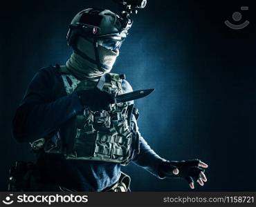 Special operations soldier, commando fighter, modern warfare combatant in combat uniform, helmet with night-vision, wearing mask and glasses, sneaking in darkness for sentry quiet removal with knife. Commando fighter creeping in darkness with knife