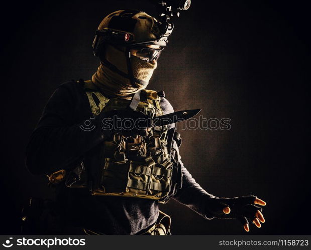 Special operations soldier, commando fighter, modern warfare combatant in combat uniform, helmet with night-vision, wearing mask and glasses, sneaking in darkness for sentry quiet removal with knife. Commando fighter creeping in darkness with knife