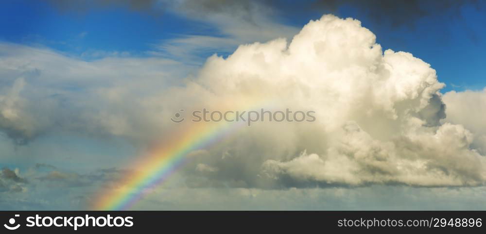 Spectacular rainbow in bright colors rising up to a huge white cloud with blue sky