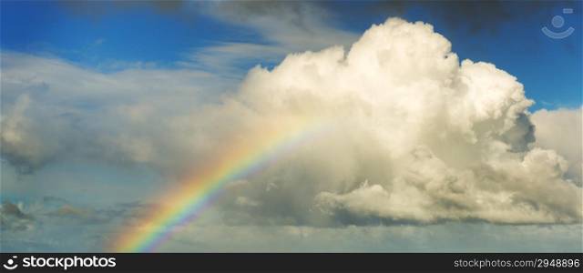 Spectacular rainbow in bright colors rising up to a huge white cloud with blue sky