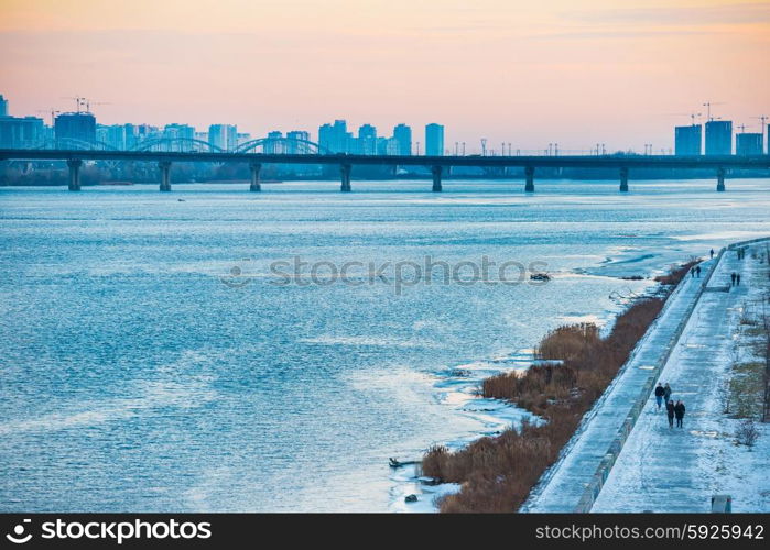 Spectacular sunset city view with bridge over Dnepr river. People walking on the wharf. Kiev, Ukraine