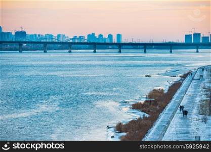 Spectacular sunset city view with bridge over Dnepr river. People walking on the wharf. Kiev, Ukraine