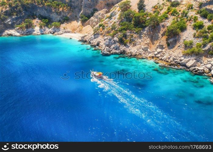 Speed boat in blue sea at sunrise in summer. Aerial view of floating motorboat in sea bay. Tropical landscape with yacht, clear water, rocks , stones, mountain, green trees. Top view. Oludeniz, Turkey