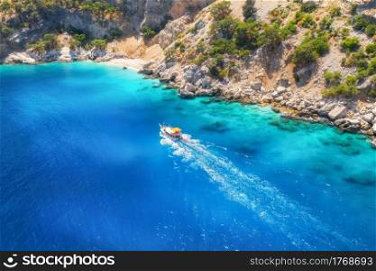 Speed boat in blue sea at sunrise in summer. Aerial view of floating motorboat in sea bay. Tropical landscape with yacht, clear water, rocks , stones, mountain, green trees. Top view. Oludeniz, Turkey
